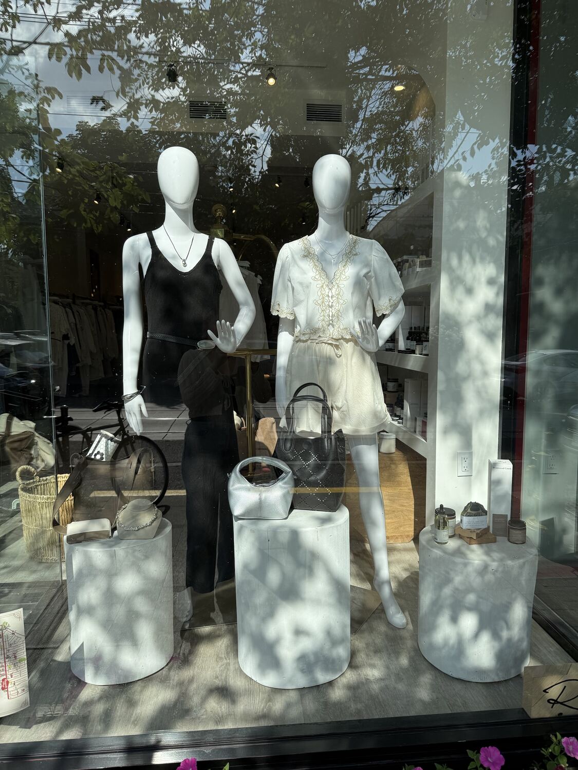 A shop window with two mannequins in black and ivory, with handbags and jewellery on white plinths