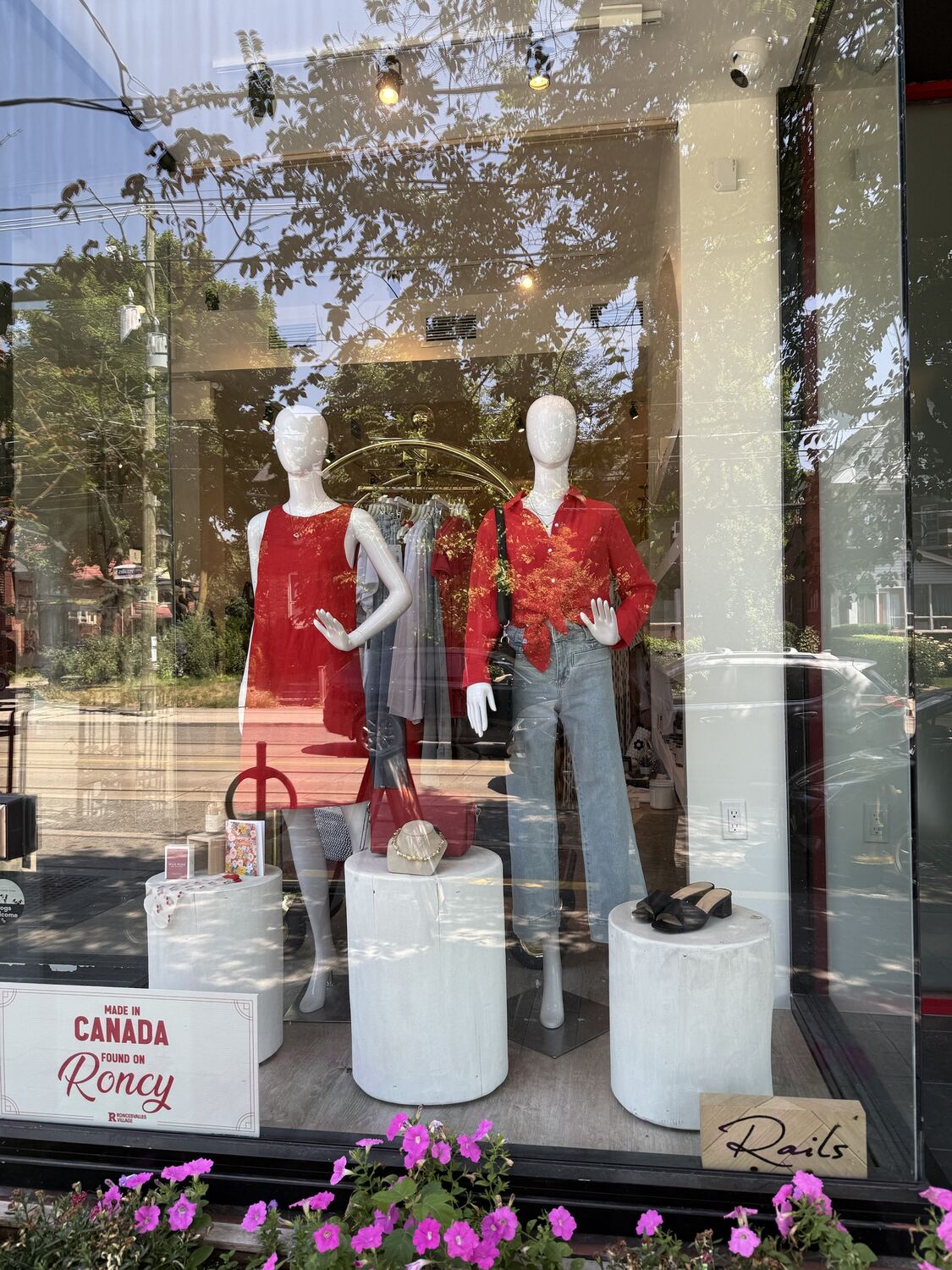 A shop window with two mannequins in red and denim, white plinths and a Made in Canada sign
