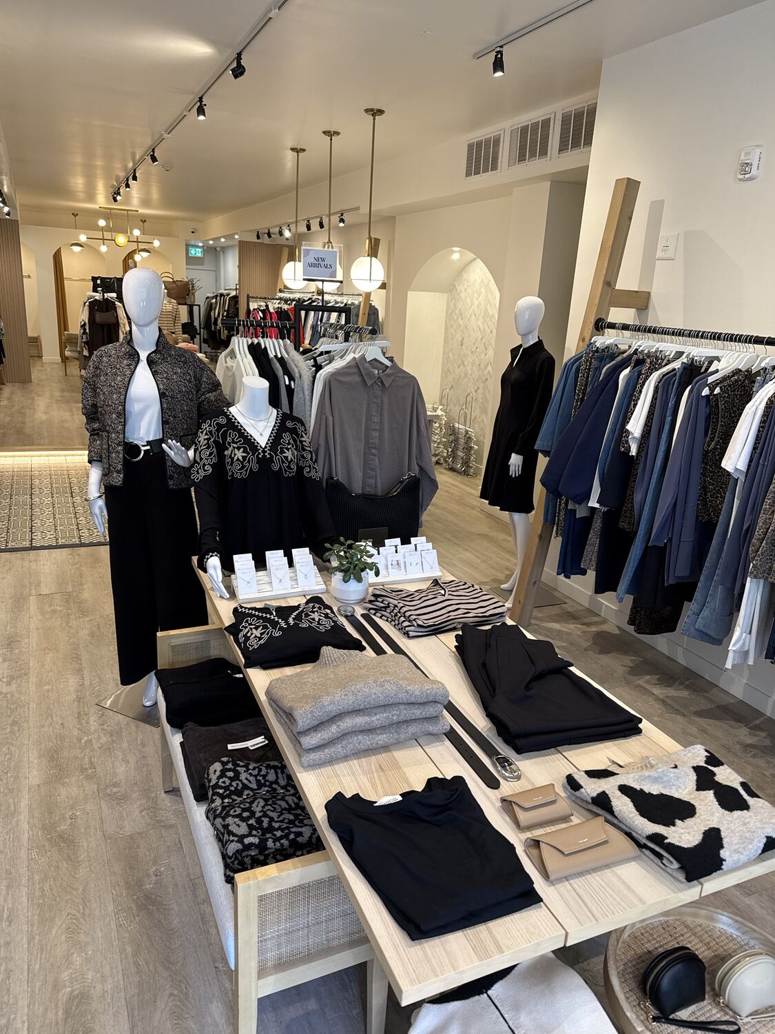 A shop floor with mannequins and a table of black, grey and leopard pieces, with a rail of denim on the right